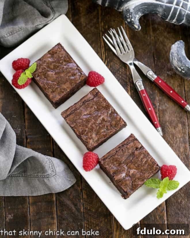 3 sheet pan brownies on a white tray with fresh raspberries and mint sprigs, highlighting their dessert potential.