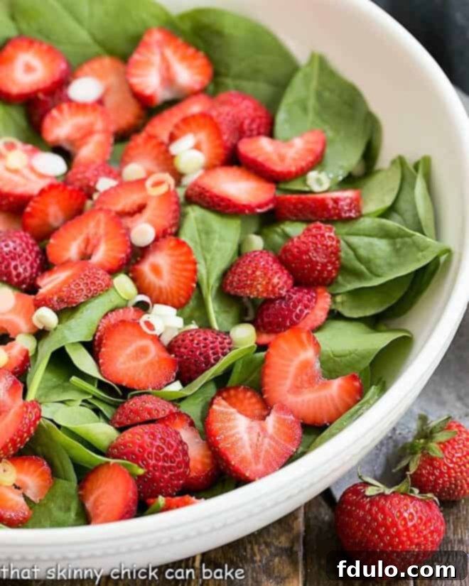 Undressed Strawberry Spinach Salad in a white serving bowl, showcasing fresh spinach and sliced strawberries.