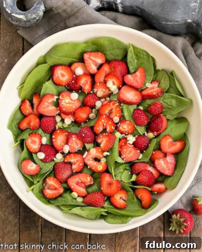 Overhead view of an easy strawberry spinach salad in a white ceramic bowl, garnished and ready to serve.