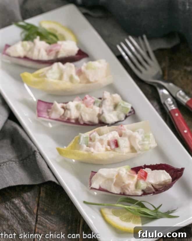 Artfully presented Lobster Salad in Endive Cups on a white serving tray, accompanied by small, elegant red-handled forks, inviting guests to savor this refined appetizer.