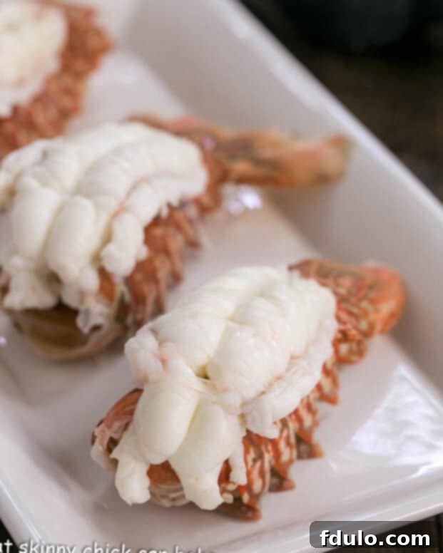 A selection of perfectly cooked lobster tails arranged neatly on a pristine white tray, showcasing their vibrant color and readiness for meat extraction and inclusion in the salad.