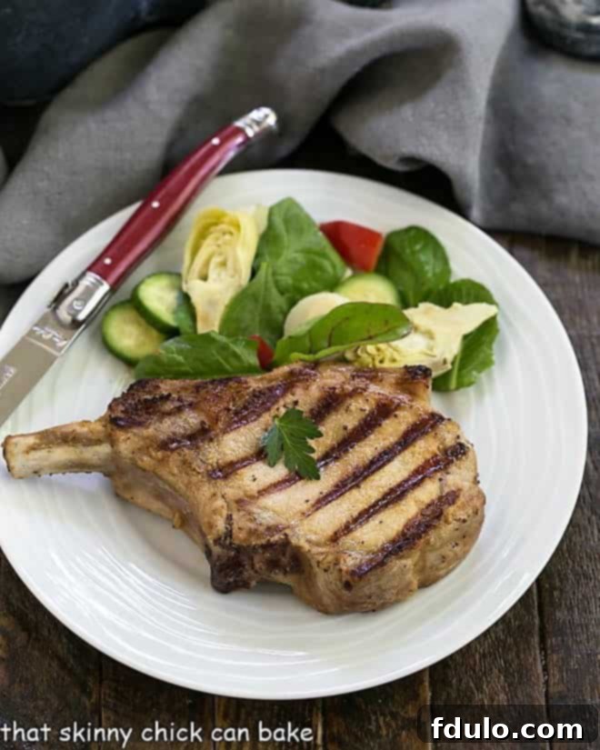 Overhead view of marinated pork chop with a salad on a white plate, highlighting a perfectly grilled piece of meat.