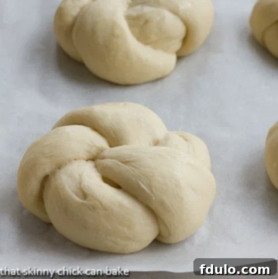 Several unbaked Yeast Roll Knots arranged neatly on a parchment-lined baking sheet, waiting to proof and expand before baking.
