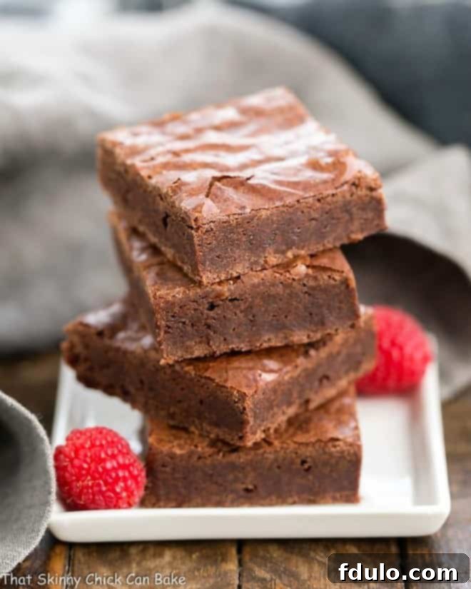 A stack of two rich, fudgy brownies presented on a pristine white square plate, highlighting their perfect texture.