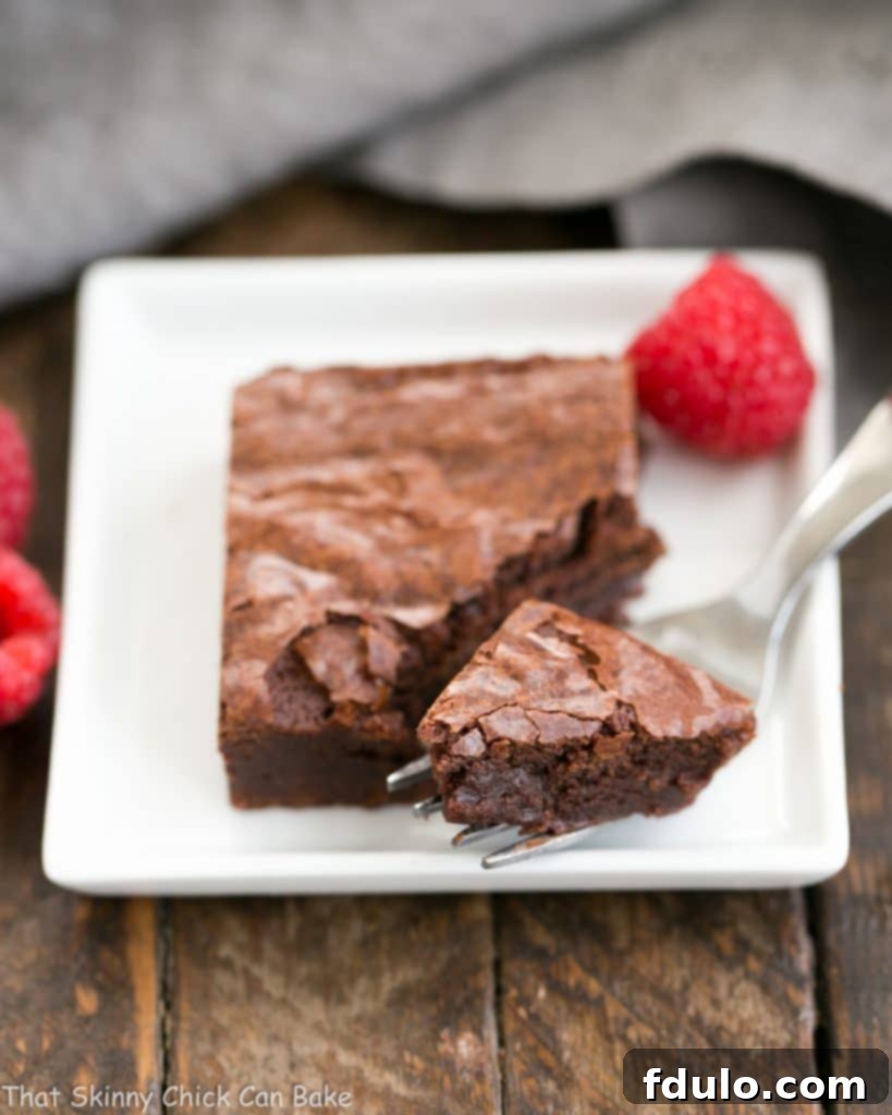 A perfectly sliced fudgy brownie on a square plate, with a fork removing a small bite, showcasing its dense and moist interior.