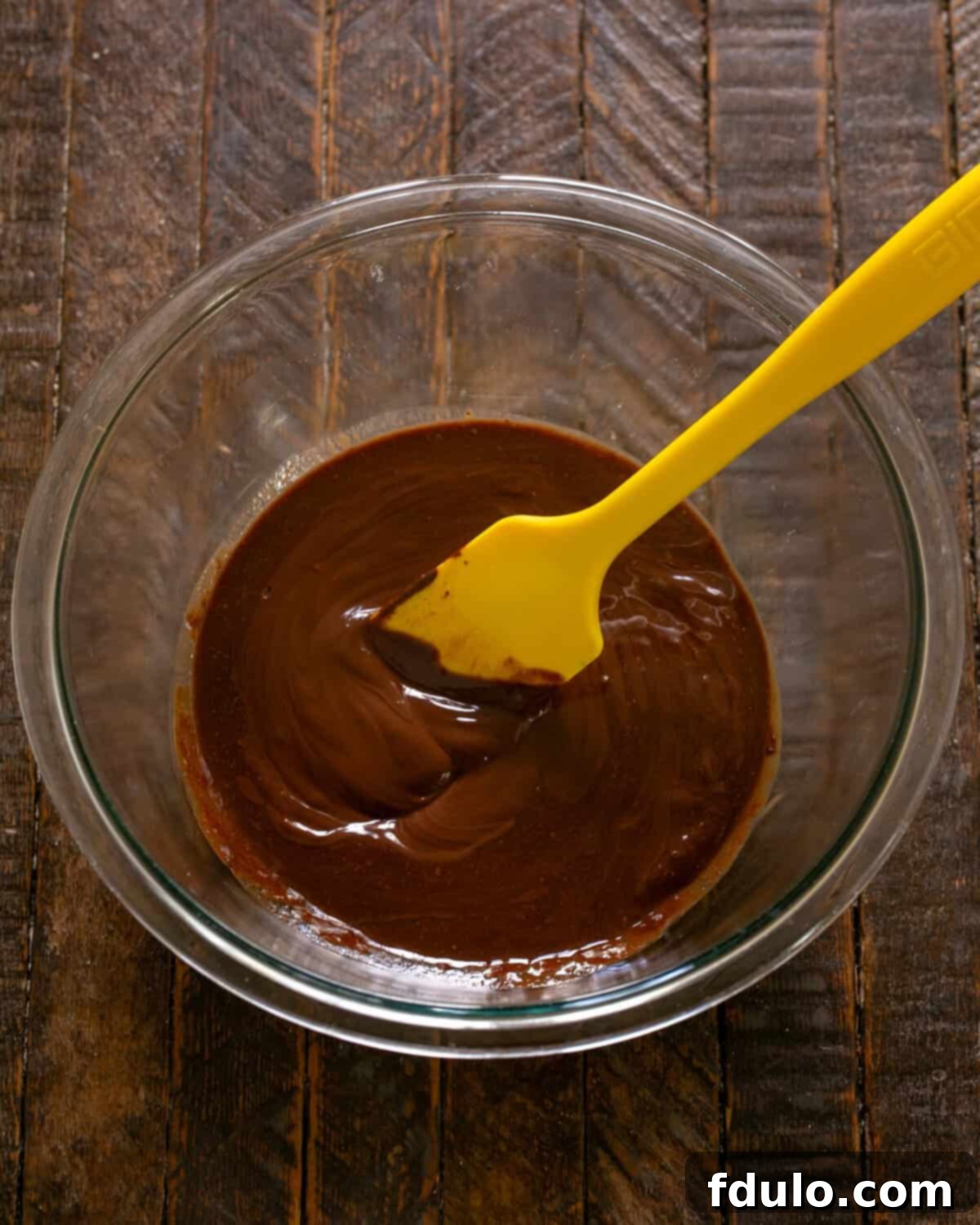 Step-by-step image showing the melted chocolate and butter being stirred until smooth and combined.