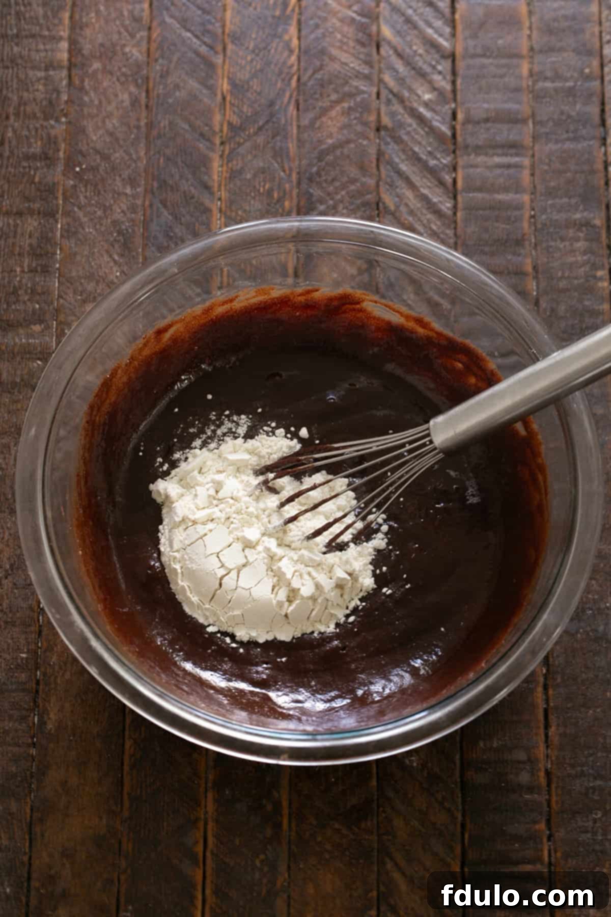 Step-by-step image showing flour being added to the brownie batter.