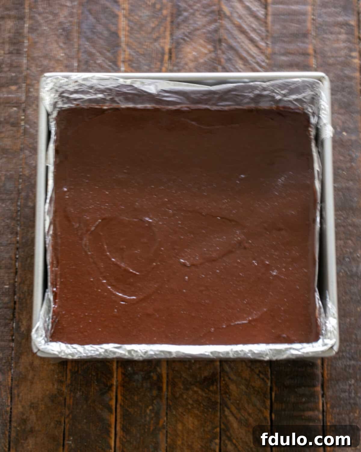 Step-by-step image showing the prepared brownie batter being spread evenly into the baking pan, ready for the oven.