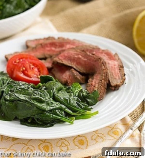 A complete meal featuring succulent flank steak paired with a generous portion of quick and easy lemon-steamed spinach on a white dinner plate.