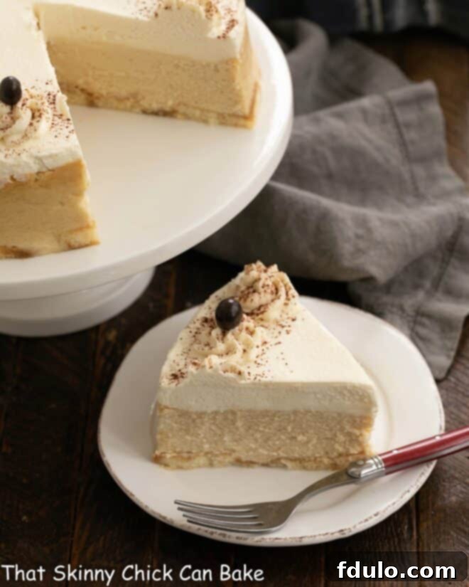 A perfectly portioned slice of Tiramisu Cheesecake on a white dessert plate, with the remaining cheesecake beautifully in the background.