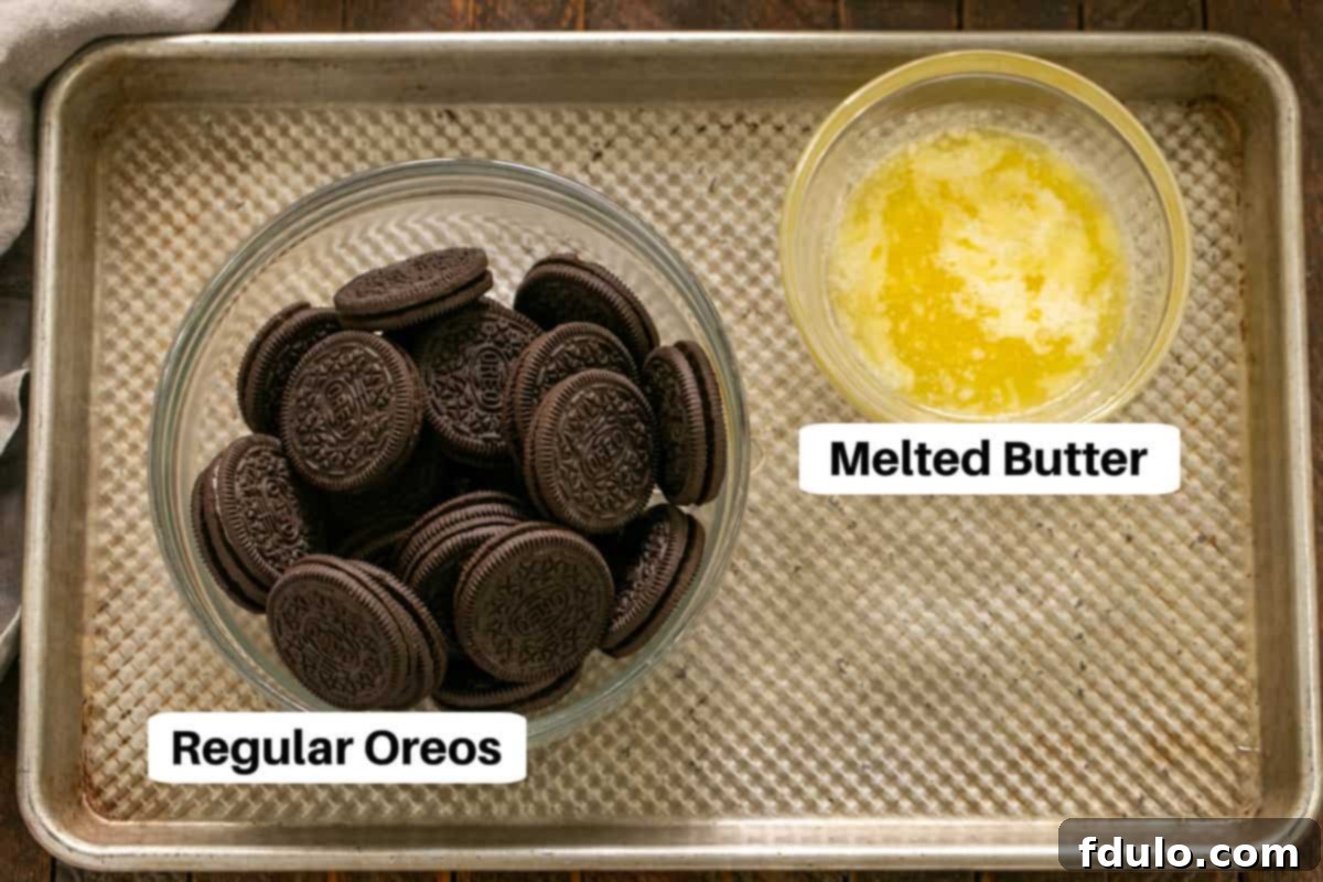 Ingredients for the Oreo crust, including whole Oreos, crushed Oreos, and melted butter, displayed on a metal sheet pan.