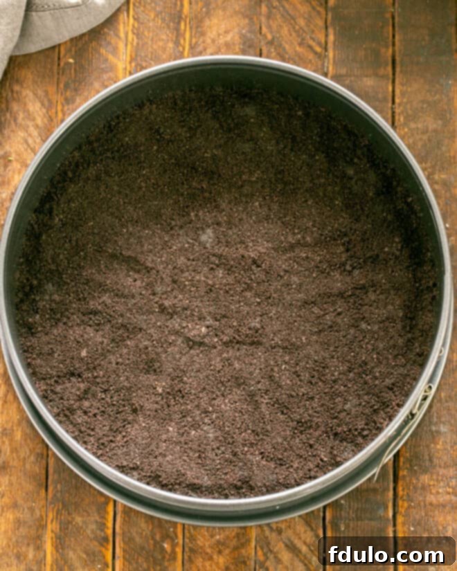 Step 1: Crushed Oreo crumbs being pressed into the bottom of a springform pan to form the crust.
