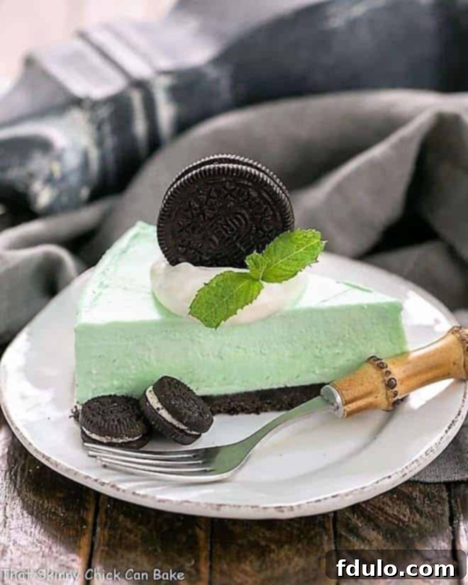 A perfectly sliced piece of frozen Grasshopper Pie with an Oreo Crust on a white dessert plate, with scattered Oreo pieces and a bamboo-handled fork.