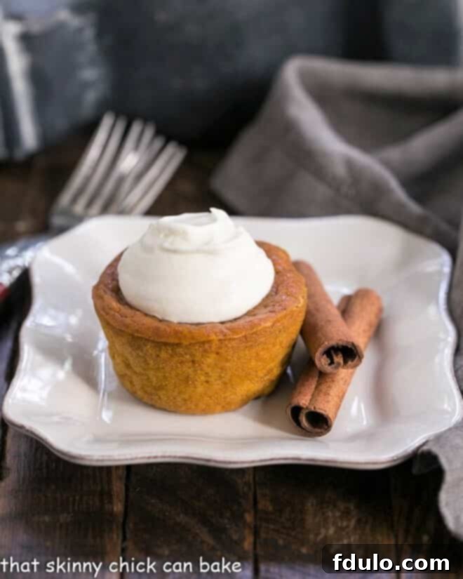 A single Pumpkin Pie Cupcake on a square white plate, elegantly topped with a generous dollop of whipped cream, ready to be enjoyed.