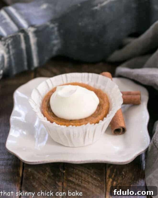 A single Pumpkin Pie Cupcake, elegantly presented in a simple white paper wrapper, placed on a square white plate, ready for serving.