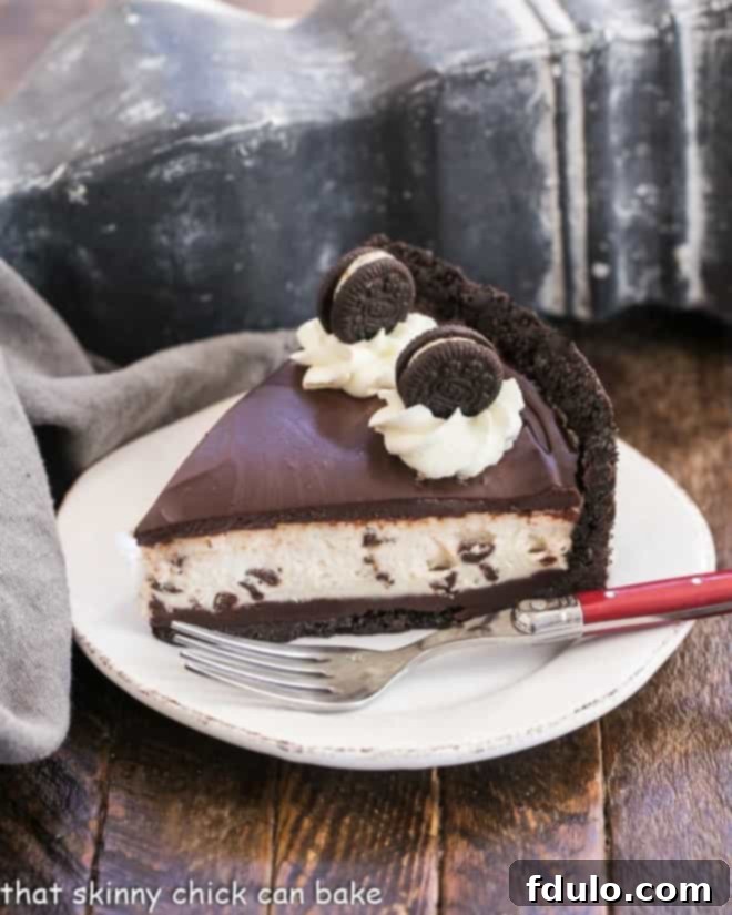 A slice of rich No-Bake Oreo Cheesecake with visible layers of crust, ganache, and creamy filling, served on a white dessert plate with a red fork.