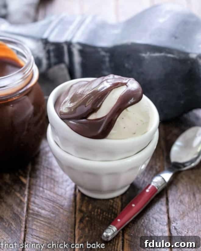 Hot Fudge Sauce over a scoop of vanilla ice cream in stackeed white bowls. A spoonful of hot fudge is being drizzled.