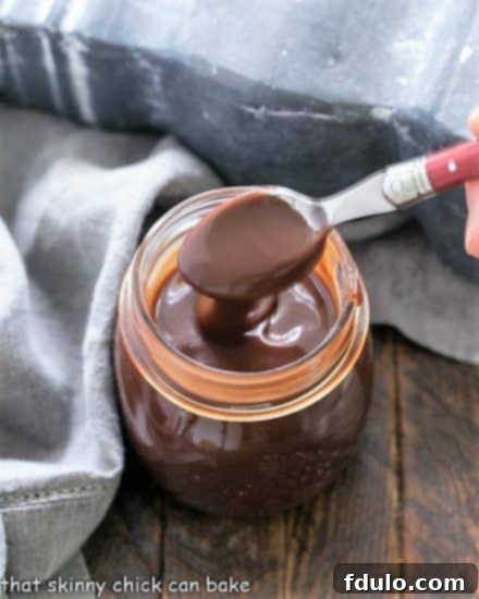 Jar of homemade hot fudge sauce with a spoonful being removed, showcasing its thick, rich texture.