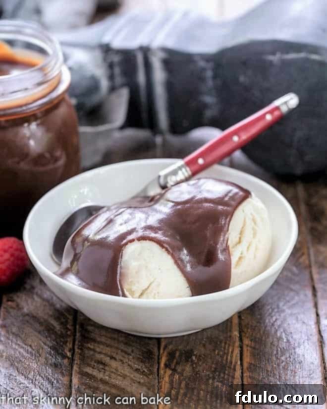 A bowl of vanilla ice cream topped with hot fudge sauce and a red handled spoon, ready to be enjoyed.