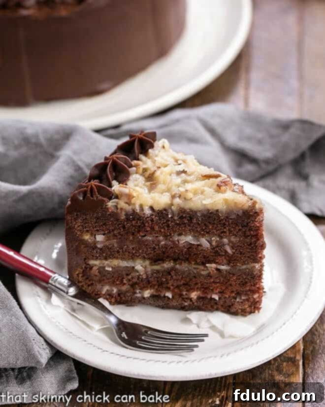 A perfectly sliced piece of German Chocolate Cake on a white dessert plate, revealing its beautiful four layers and rich filling, with the whole cake partially visible in the background.