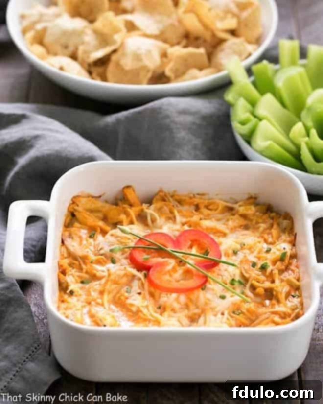Creamy Buffalo Chicken Dip in a rustic baking dish, beautifully garnished with fresh green chives and a vibrant red bell pepper slice, ready for serving.