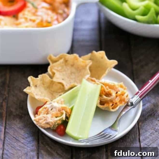 A serving of hot Buffalo Chicken Dip on a small appetizer plate, accompanied by crisp tortilla chips and fresh celery sticks for dipping.