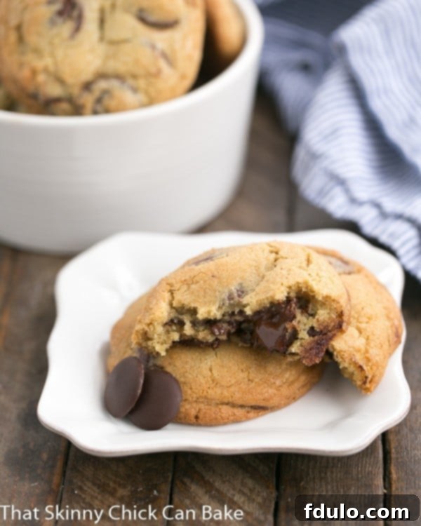 The New York Times Chocolate Chip Cookies with one broken open on a white square plate, revealing the melted chocolate within.