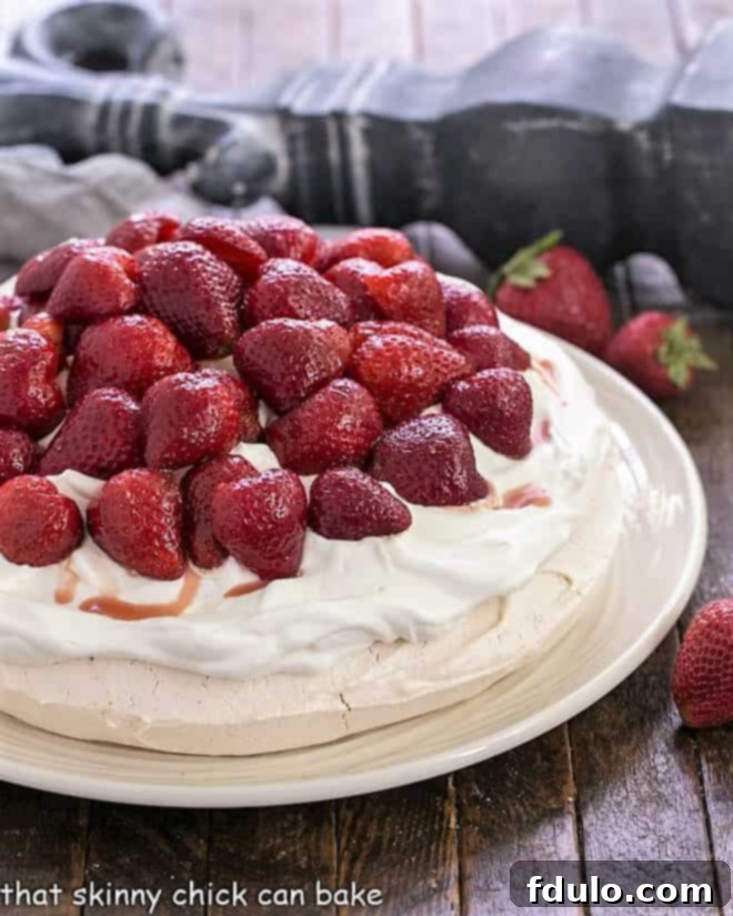A stunning Strawberry Pavlova on a white serving plate, generously topped with halved fresh strawberries and a billowy mound of whipped cream, ready to be served.