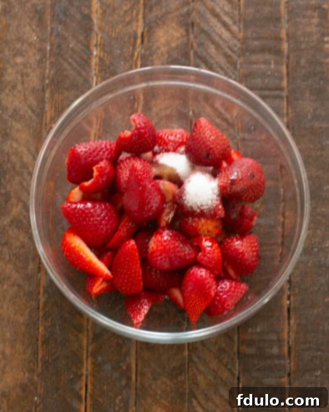 Fresh strawberries being combined with vanilla extract, balsamic vinegar, and sugar in a mixing bowl, creating the delicious balsamic strawberry topping.