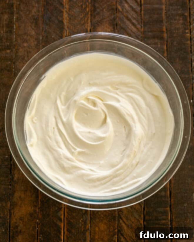 Heavy cream and sugar being whipped in an electric mixer until thick and able to hold firm peaks, preparing the luscious whipped cream topping.