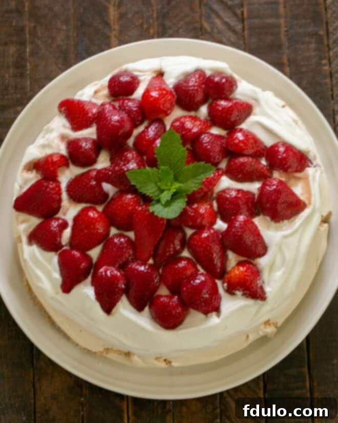 The cooled meringue base topped with a generous layer of whipped cream, followed by the balsamic strawberries, illustrating the final assembly of the Strawberry Pavlova.