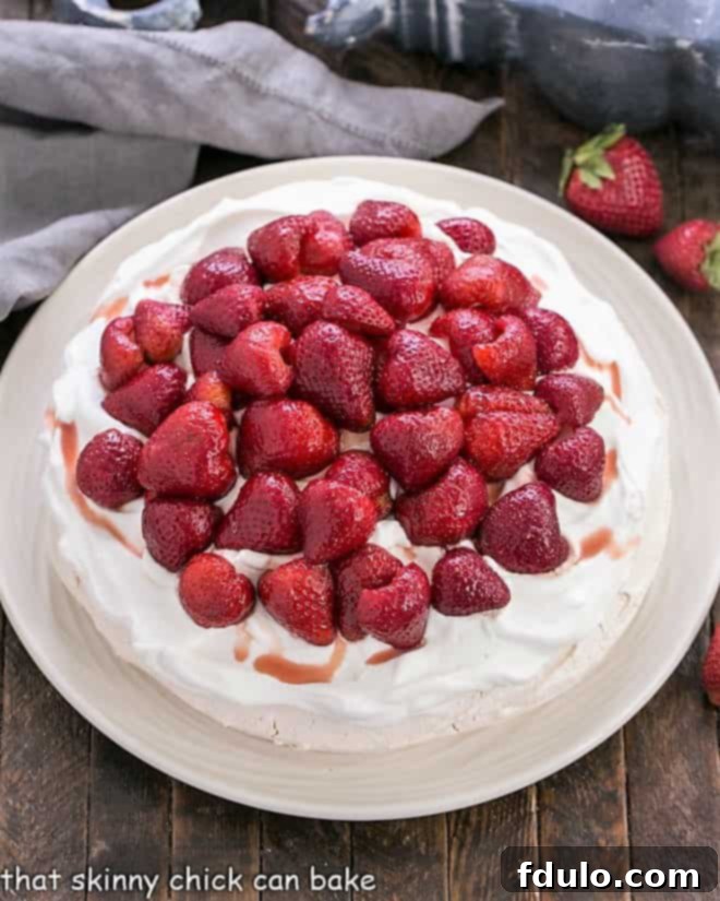 An overhead view of a beautifully assembled Strawberry Pavlova, showcasing its generous whipped cream topping and artfully arranged fresh strawberries on a white serving plate.