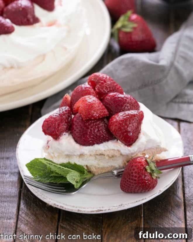 A perfectly sliced piece of Strawberry Pavlova on a dessert plate, elegantly garnished with a fresh mint sprig, showcasing the meringue's texture, whipped cream, and balsamic strawberries.