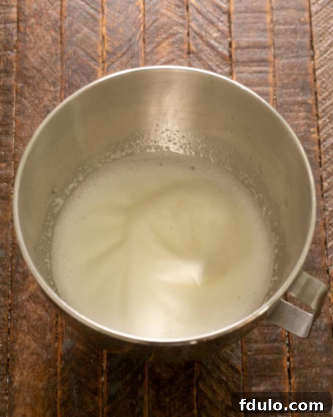 Egg whites and a pinch of salt being beaten in an electric mixer until they form soft peaks, indicating the start of the meringue-making process.