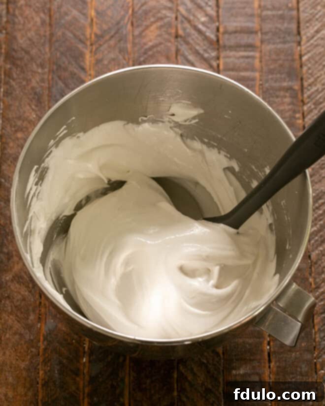Cornstarch, white-wine vinegar, and vanilla extract being gently folded into the stiff meringue mixture, enhancing its stability and flavor.