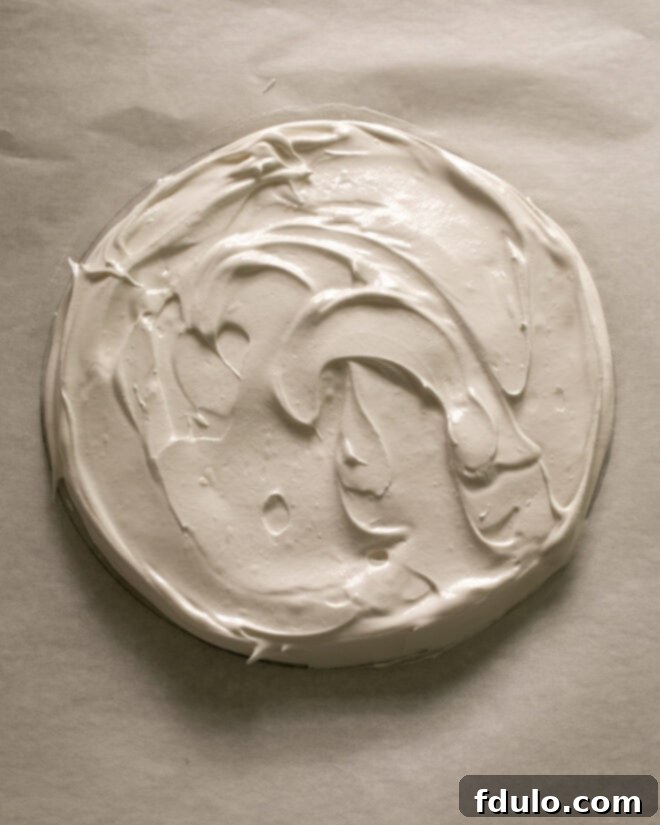 The prepared meringue mixture being spread evenly within the traced circle on the parchment paper, forming the base of the pavlova.