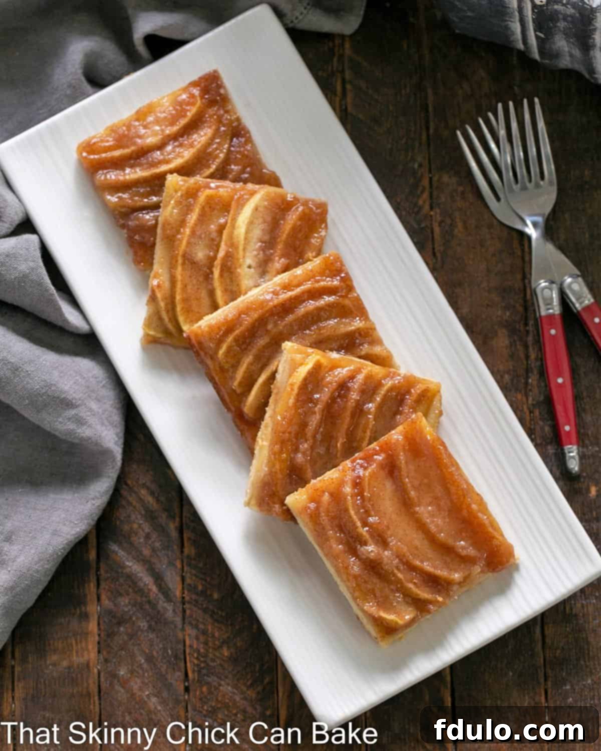 A white platter filled with perfectly cut squares of warm German Apple Kuchen, ready to be served.
