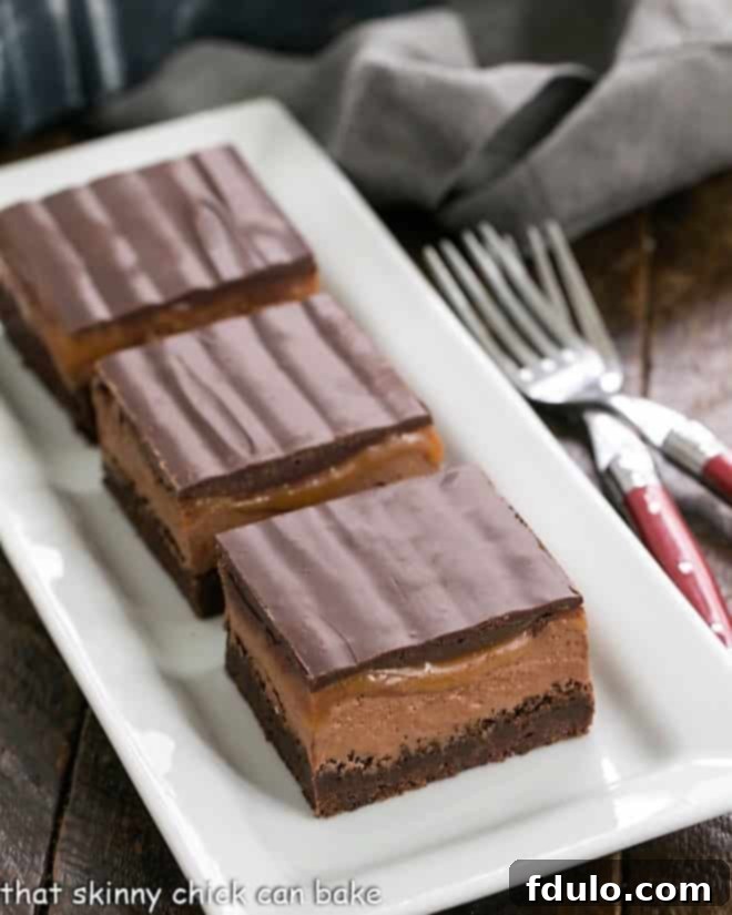 Three decadent Milky Way Brownies artfully arranged on a pristine white ceramic tray, showcasing their irresistible layers of chocolate and caramel.