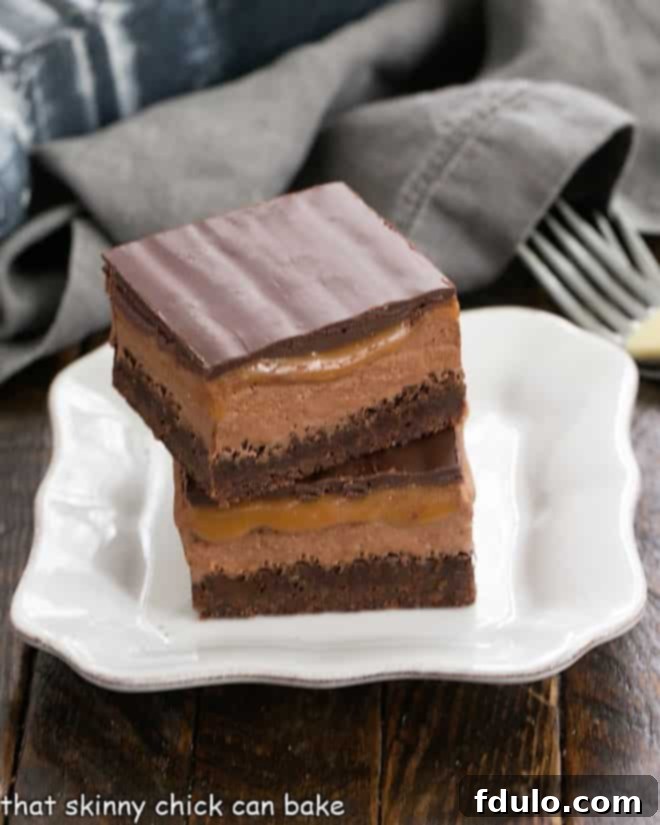 A perfectly stacked duo of Milky Way Brownies rests on a pristine white plate, highlighting their distinct, delicious layers.