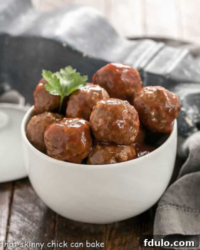 Close-up of Cranberry Cocktail Meatballs glistening in a white ceramic bowl, garnished with fresh cranberries.