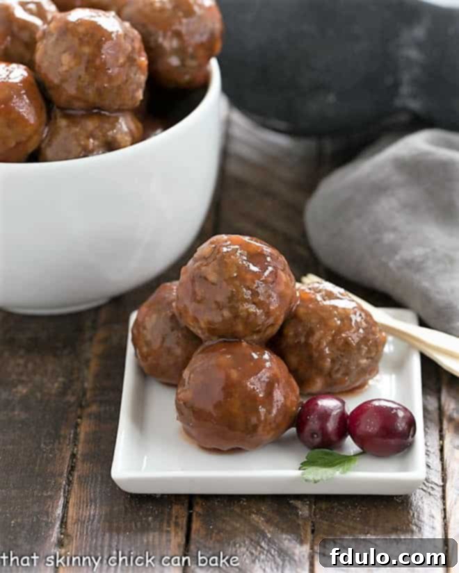 Platter of golden-brown baked meatballs, garnished with a sprig of fresh parsley and a couple of vibrant red cranberries.