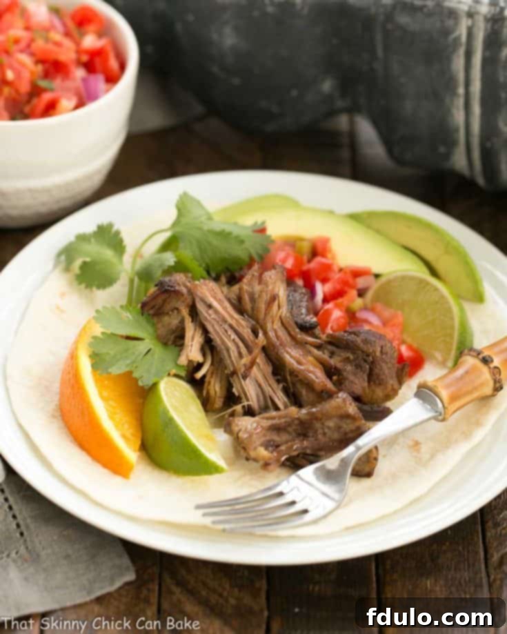 Slow cooked Pork Carnitas over a tortilla on a white plate