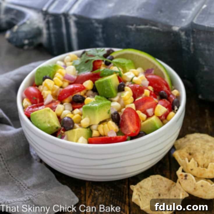 White ceramic serving bowl filled with corn salsa next to a few corn chips