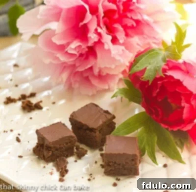 A nearly empty platter of perfectly dense and decadent Frosted Chocolate Chocolate Chip Brownies, adorned with pink peonies