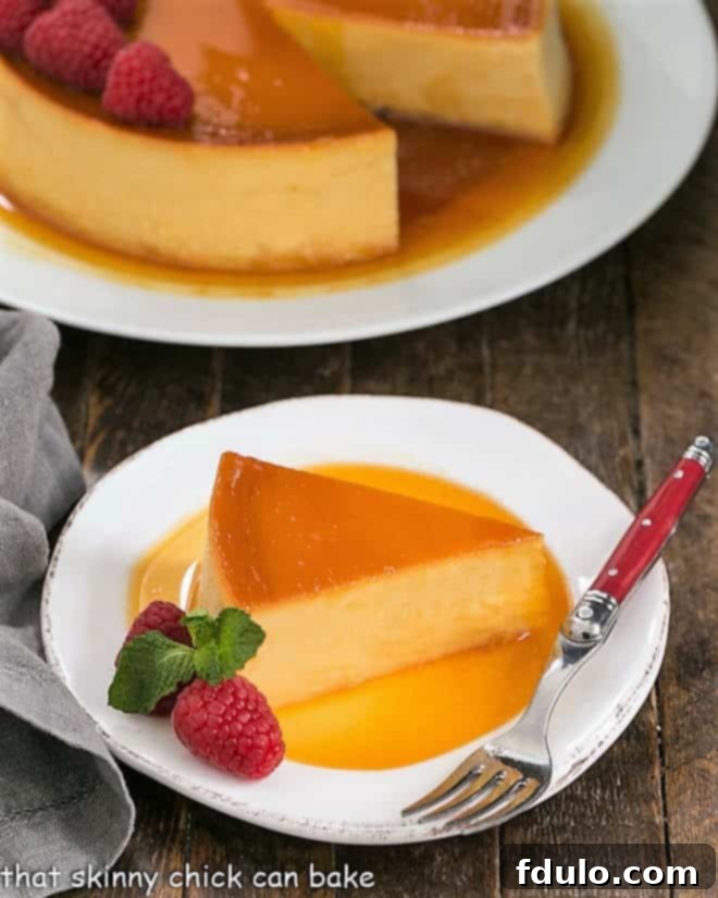 A perfectly sliced piece of Leche Flan on a white plate, garnished with fresh raspberries, highlighting its smooth texture and rich caramel.