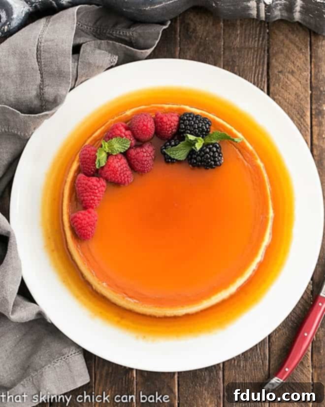 Overhead view of a perfectly inverted Cream Cheese Flan on a white serving plate, with caramel pooling around the edges.