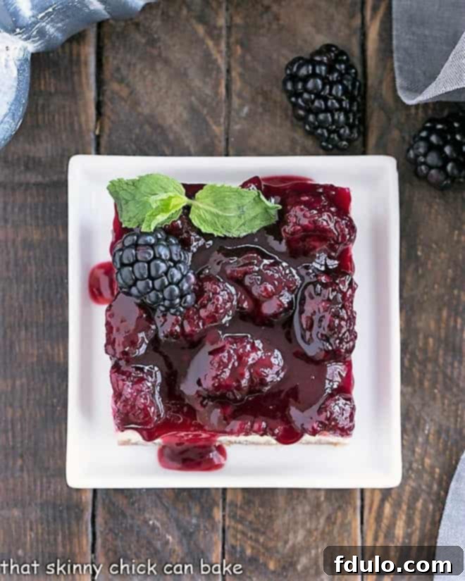 Overhead view of a blackberry cheesecake bar on a square white plate with a sprig of mint