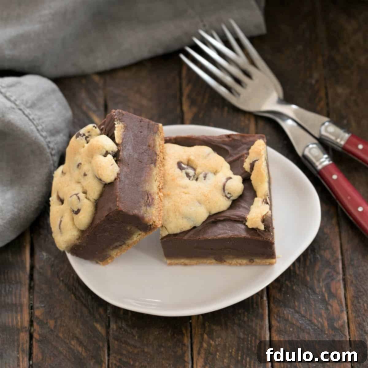 Two perfectly cut slices of Fudge and Toffee Filled Chocolate Chip Bars on a delicate oval plate, accompanied by two forks, ready to be enjoyed.