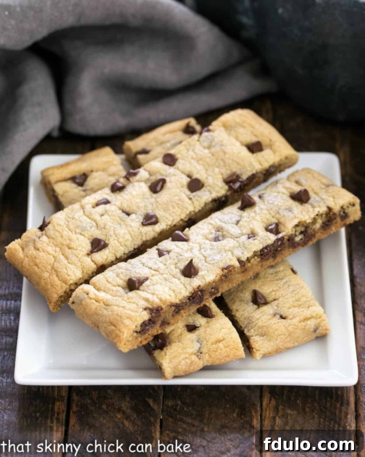 Four golden-brown chocolate chip cookie sticks resting on a square white plate, perfectly baked with melted chocolate chips visible.