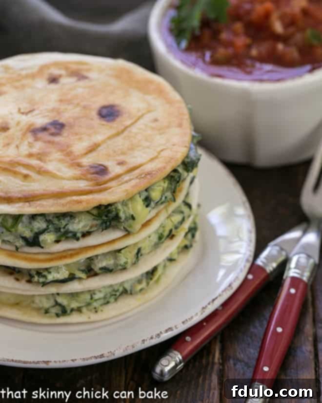 A stack of homemade spinach dip quesadillas on a white plate, garnished with fresh cilantro and served with a side of vibrant red salsa, ready for enjoyment.
